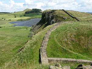 A stone wall on a hill with Hadrian's Wall in the background

Description automatically generated